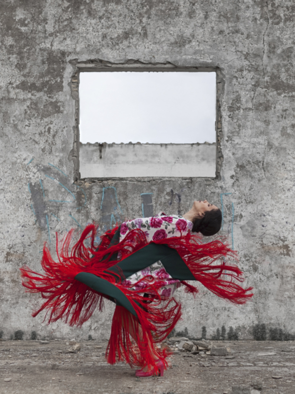 Danza tradicional frente a un muro con ventana, con vestimenta colorida y flores.