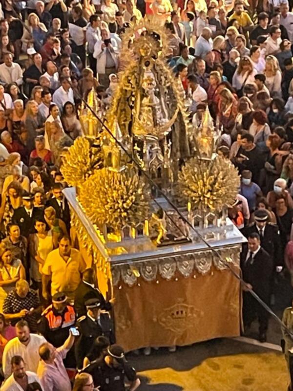 Procesión religiosa con imagen dorada en el centro, rodeada por una multitud en una noche festiva.