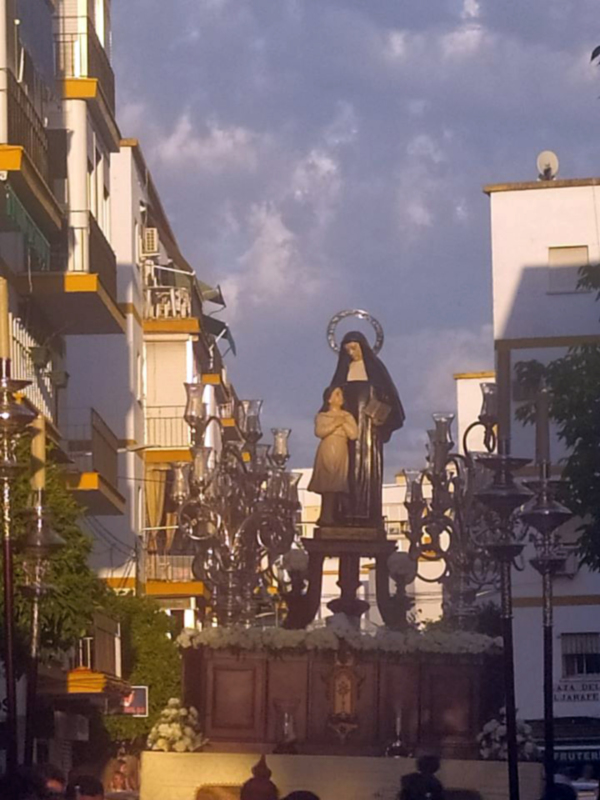 Procesión religiosa con estatua de la Virgen y Niño, adornada con candelabros y flores, en una calle urbana.