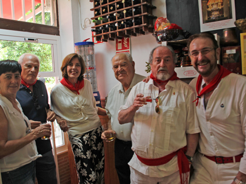 Celebración en un bar con camareros vestidos de blanco y rojo, disfrutando de una copa de vino.