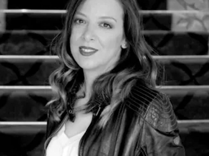 Retrato en blanco y negro de una mujer con chaqueta de cuero, fondo de estantería de ropa.