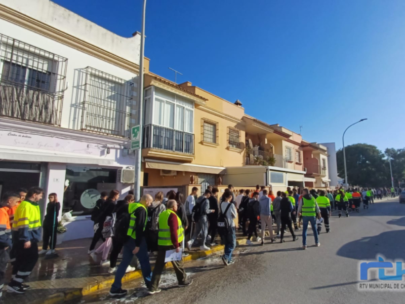 Una multitud de personas con chalecos amarillos y cascos verdes se congrega en una calle, probablemente durante un evento o protesta. La imagen muestra edificios residenciales y una calle con señales de tráfico, iluminada por el sol.