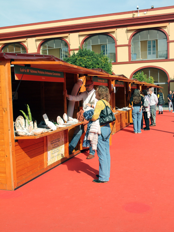 Mercado artesanal con stands de cerámica y visitantes en un día soleado.