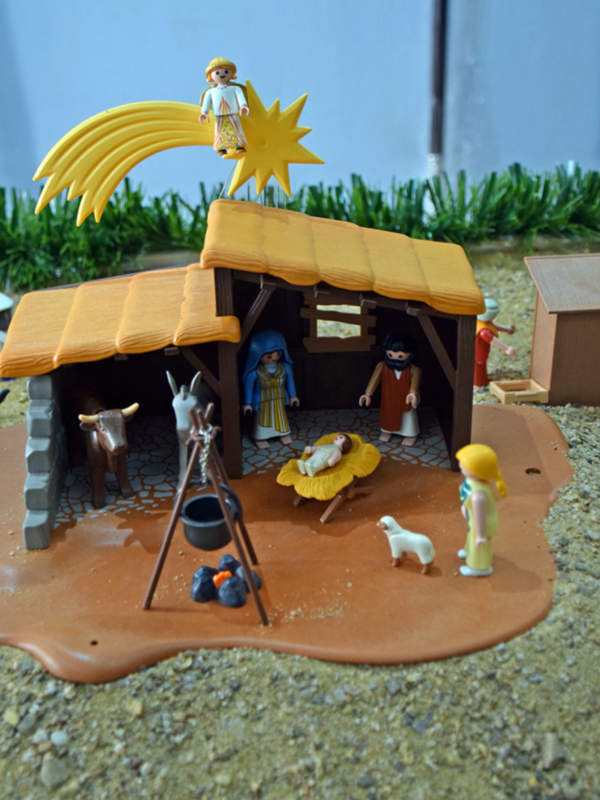 Un adoratorio de Playmobil con un establo, un niño, un pastor y un rebaño, todo en un entorno de pizarra y césped artificial.