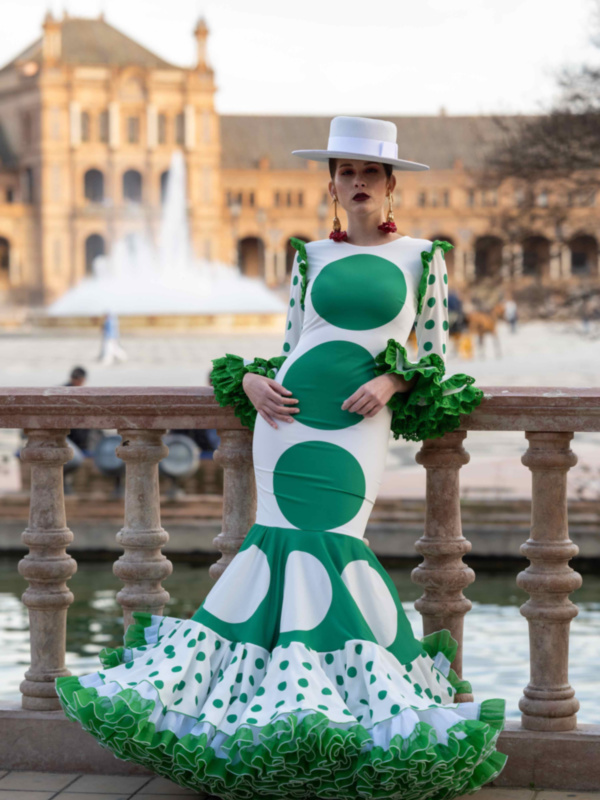 Retrato de una mujer vestida con un traje de flamenca blanco y verde, posando frente al Palacio de España de Sevilla.
