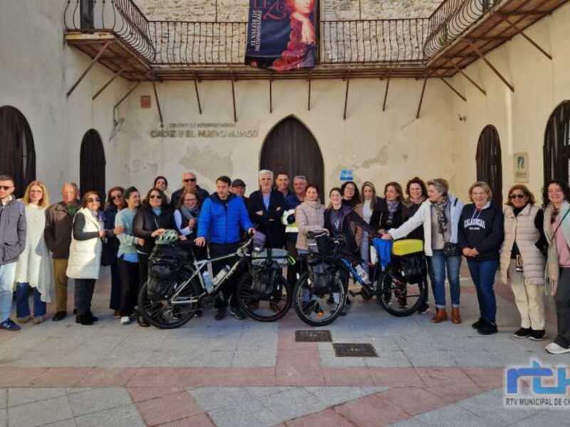 Gruppo di ciclisti posa per un gruppo di foto davanti a un edificio storico con iscrizioni sulla facciata.