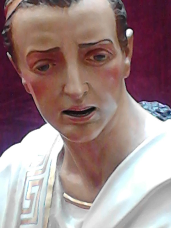 Cabeza de estatua de hombre con expresión serena, vestido con túnica blanca y detalles dorados.