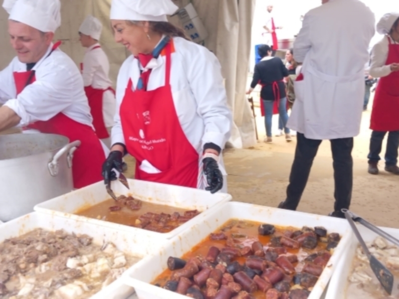 Cocineros preparando deliciosa comida en un evento al aire libre, con cubiertos y alimentos en recipientes.