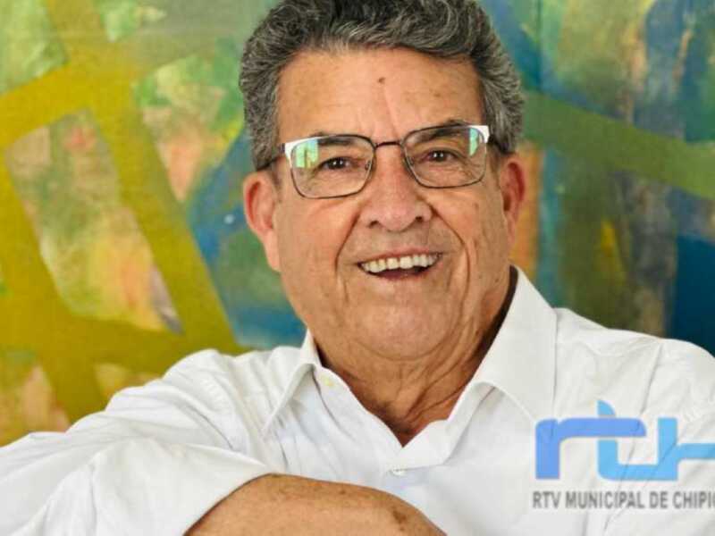 Retrato de hombre sonriente con camisa blanca y fondo abstracto de colores vibrantes.