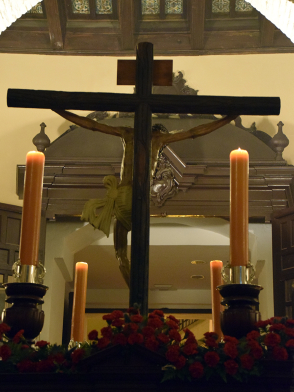 Cristo en la cruz con velas y flores rojas en el altar de una iglesia.