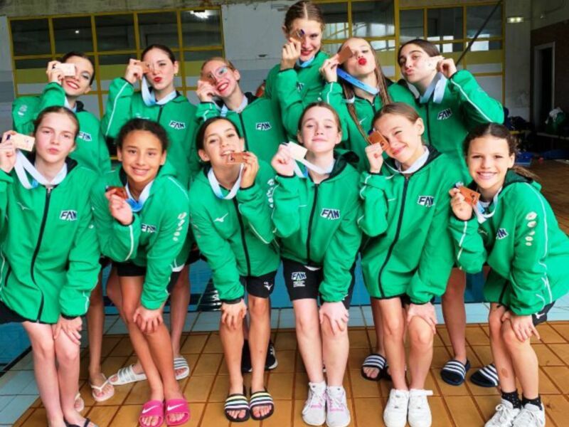 Una escuela de natación muestra orgullosas sus medallas en la piscina.