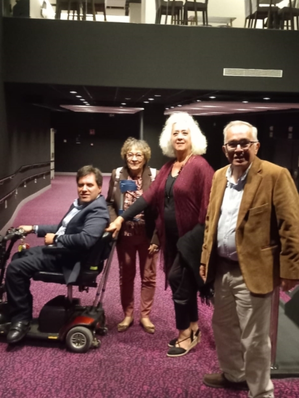 Una familia de cuatro personas, incluyendo un hombre en silla de ruedas, posa juntos en una sala con alfombra púrpura y estructura de madera.