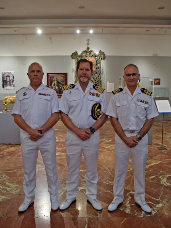 Tres oficiales en uniforme blanco posan en un museo con arte y decoración histórica al fondo.