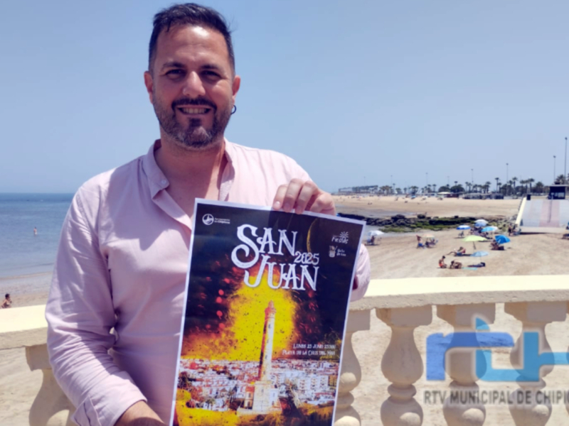 Hombre sosteniendo el cartel de la Feria de San Juan 2025 en Chipiona, con vista a la playa.
