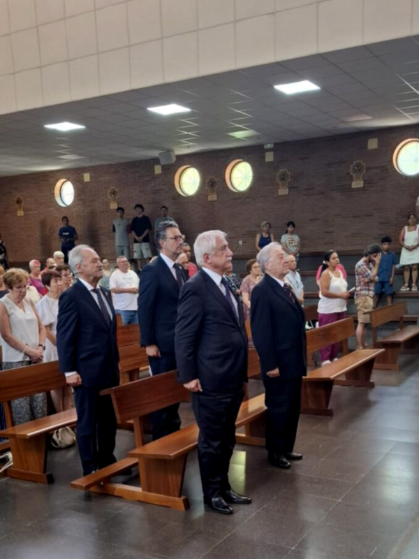 Un grupo de personas en trajes formales se encuentran en una sala con bancas y luces redondas.