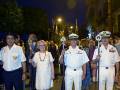 Oficiales y autoridades en uniforme blanco participan en una ceremonia nocturna en una calle urbana.