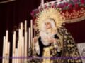 Una procesión religiosa con una figura vestida en traje tradicional, posiblemente una imagen de la Virgen, rodeada por velas y adornos florales. La hermandad se identifica como "Hermándad de la Salle".