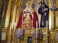 Altar de una iglesia con estatua de la Virgen María y un soldado en uniforme. En el fondo, una arquitectura dorada con detalles artísticos y flores en las mesas.