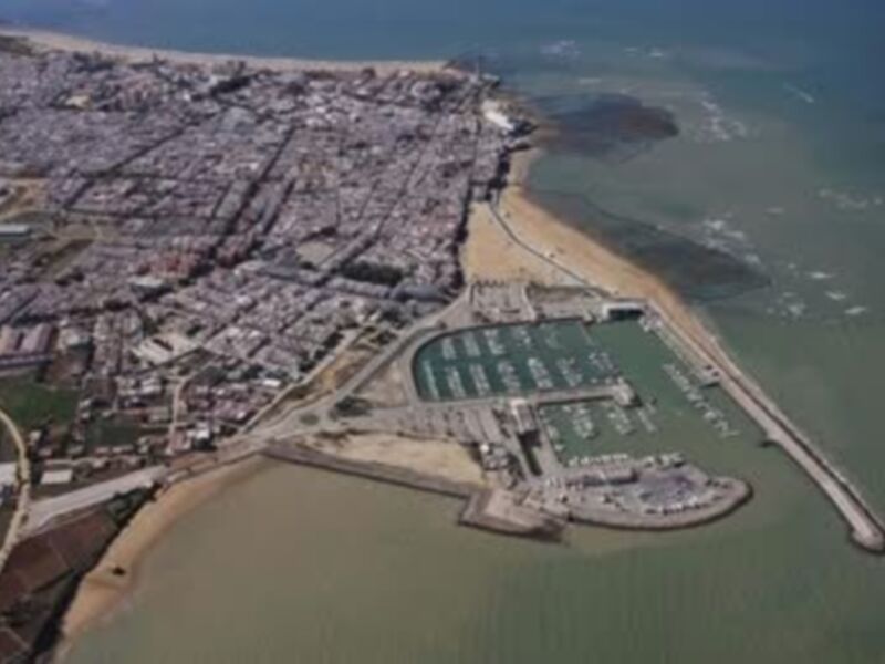 Imagen aérea de una ciudad costera con un puerto y playas.