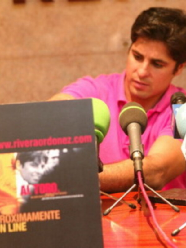 Un hombre hablando en un micrófono con una tarjeta de presentación que dice "www.riveraordonez.com" y "Proximamente On Line".