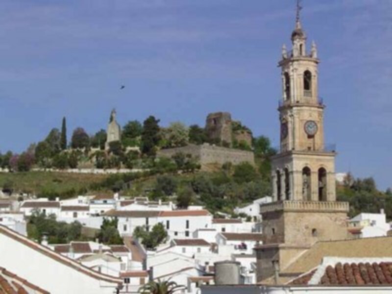 Vista panorámica de una ciudad blanca con una torre campanario y un castillo en el horizonte, bajo un cielo azul claro.