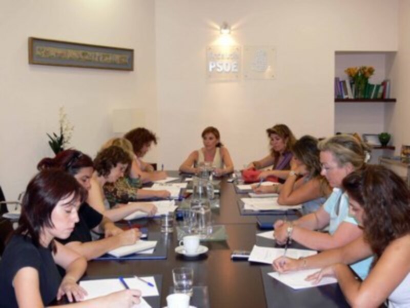 Reunión de trabajo en una sala de reuniones con varias personas sentadas alrededor de una mesa, tomando notas y discutiendo.