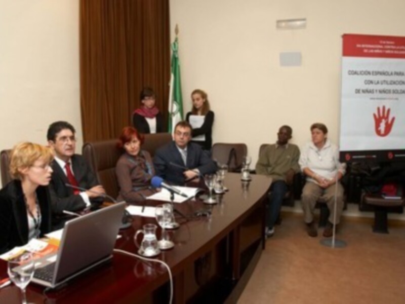 Gente en una reunión de negocios, con una mujer en el centro de la mesa, sosteniendo un documento y otros miembros de la mesa, con una pantalla en el fondo que dice 'Cultura para las personas con discapacidad'.