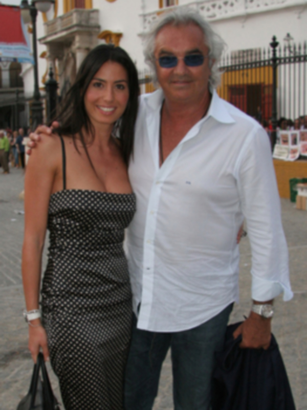 Una pareja sonríe en una calle de pueblo, con edificios históricos al fondo.