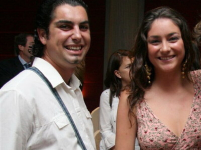 Dos personas sonrientes en un evento social, vestidas formalmente.