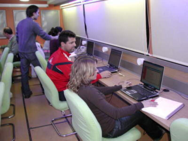 Un grupo de personas trabajando en computadoras en una sala de oficina moderna con sillas verdes y pantallas grandes.