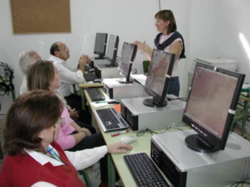 Estudiantes en una clase de informática, con computadoras y un maestro explicando.
