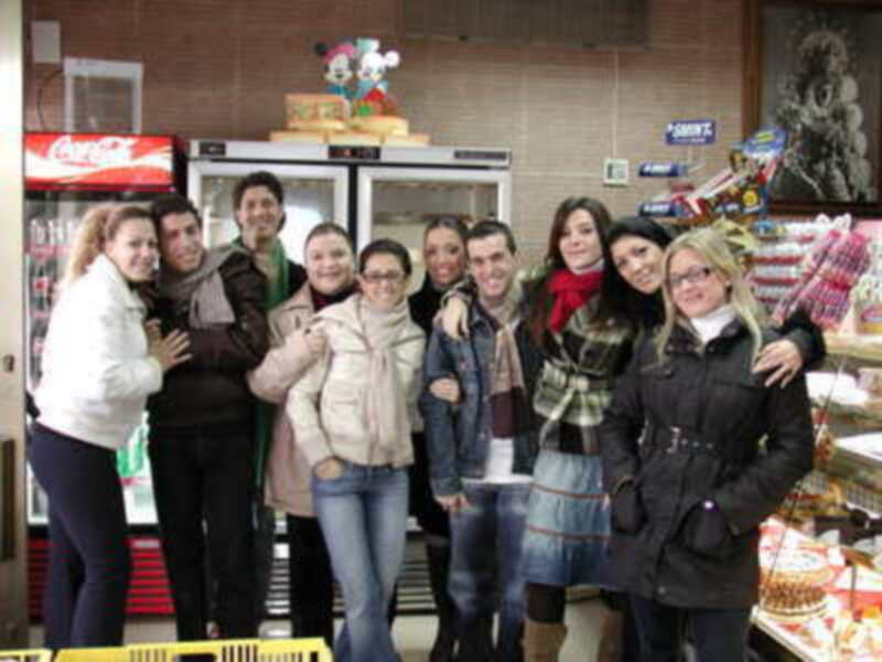 Personas sonrientes en una tienda de comestibles, frente a un refrigerador con productos y una estantería con paquetes.