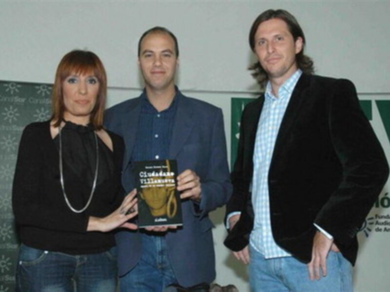 Presentación del libro "Ciudadano Villanueva" en un evento cultural, con tres personas sosteniendo el libro.