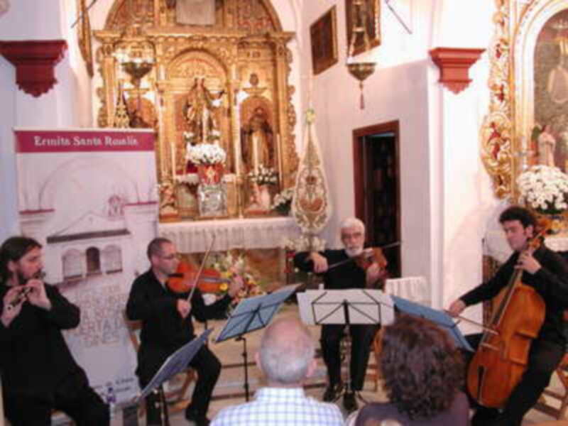 Músicos tocando violín y violonchelo en una iglesia, frente a un altar dorado con estatuas.