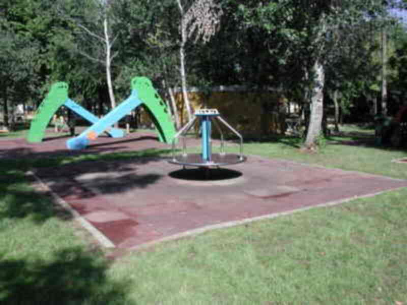 Parque infantil con columpios y roloide en césped.