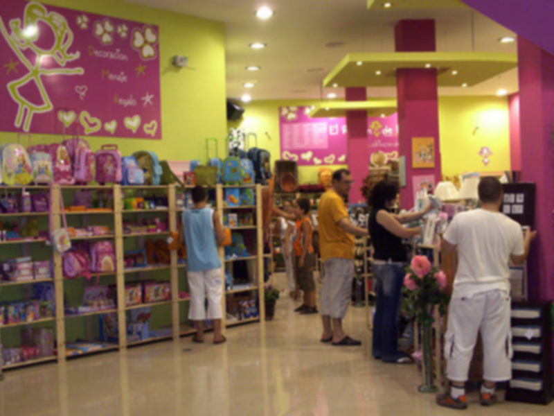Un grupo de personas en una tienda de juguetes, con estanterías llenas de juguetes y una pared decorada con dibujos animados y corazones.