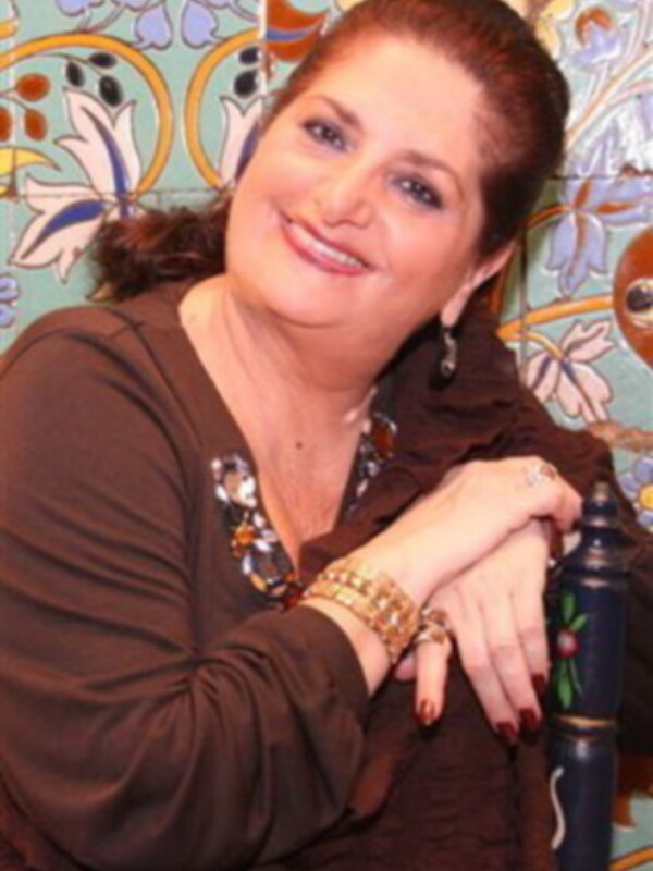 Una mujer sonriendo con un fondo de azulejos coloridos.