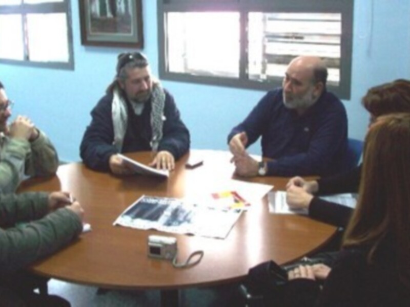 Una reunión en una oficina con personas sentadas alrededor de una mesa, sosteniendo documentos y discutiendo.