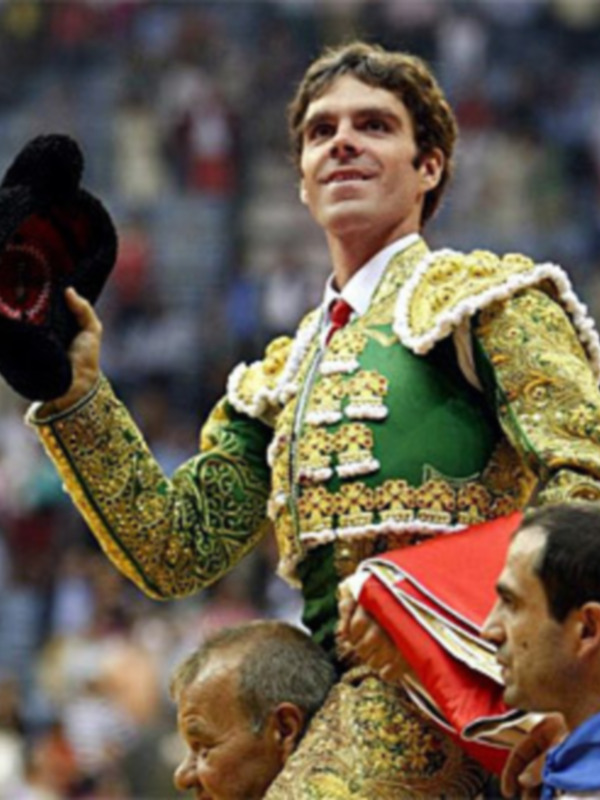 Un torero celebra en el ruedo con un sombrero en la mano, rodeado por espectadores en una corrida de toros.