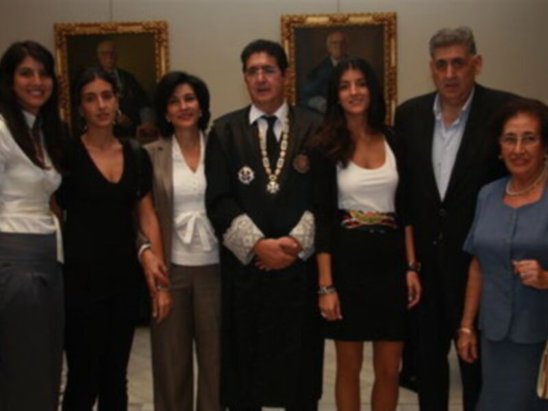 Grupo de personas posando en un evento formal en un salón con retratos enmarcados en la pared.
