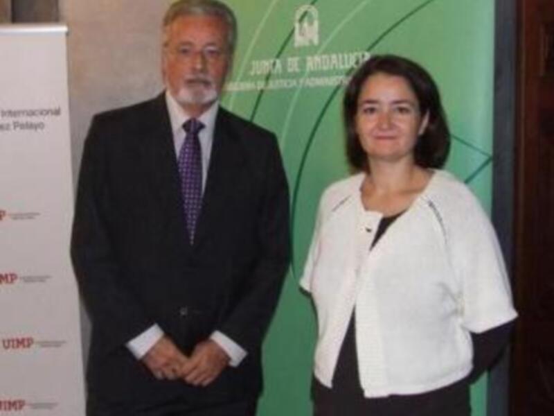 Dos personas posando frente a un cartel con el logotipo de la Junta de Andalucía y el nombre de una universidad española.