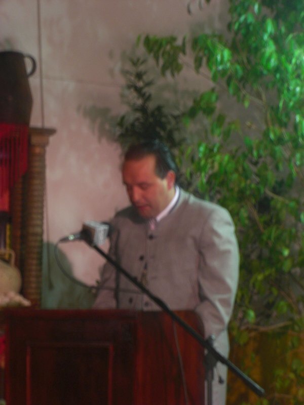 Persona hablando en un evento con micrófono y decoración botánica