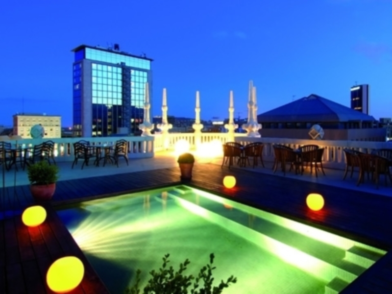 Terraza nocturna con piscina iluminada y vistas urbanas.