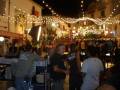Una noche festiva con luces colgantes, gente charlando y disfrutando de la música en vivo.