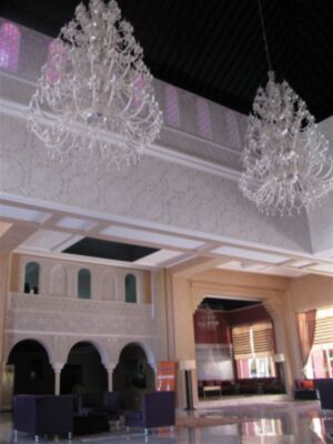 Interior de una mezquita con arcos y vitrales, dos hermosos faroles blancos en el techo.