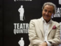 El actor se encuentra en una presentación de Teatro Quintero, sonriendo frente a un fondo negro con la imagen del actor y el nombre de la compañía.