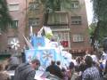 Desfile festivo con carroza temática de invierno y nieve, rodeado de espectadores en una calle urbana.