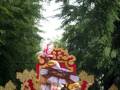 Una carroza festiva con personajes vestidos de color dorado y blanco, rodeados por adornos rojos y dorados. La carroza está decorada con elementos tradicionales, posiblemente en un evento cultural o religioso.