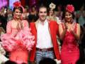 Tres modelos posan en un desfile de moda, dos con trajes flamencos y una con un vestido rojo.