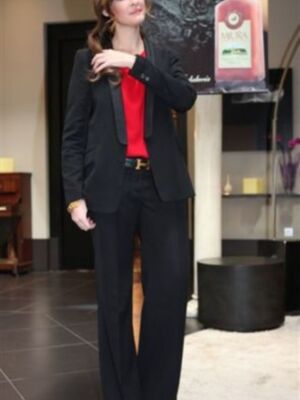 Una mujer viste un traje negro con un top rojo y una cintura plateada. Detrás, se ve una vitrina con un producto de marca.